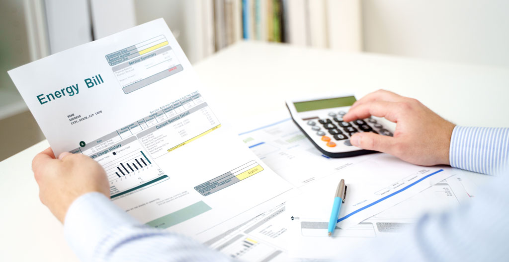 Personne assise à une table de cuisine regardant une facture papier avec une expression préoccupée, lumière naturelle de fin de journée